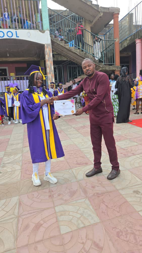 A BBBIS graduate in purple gown receiving a certificate from the Principal