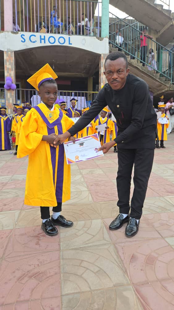 A BBBIS graduate in gold gown and cap being congratulated